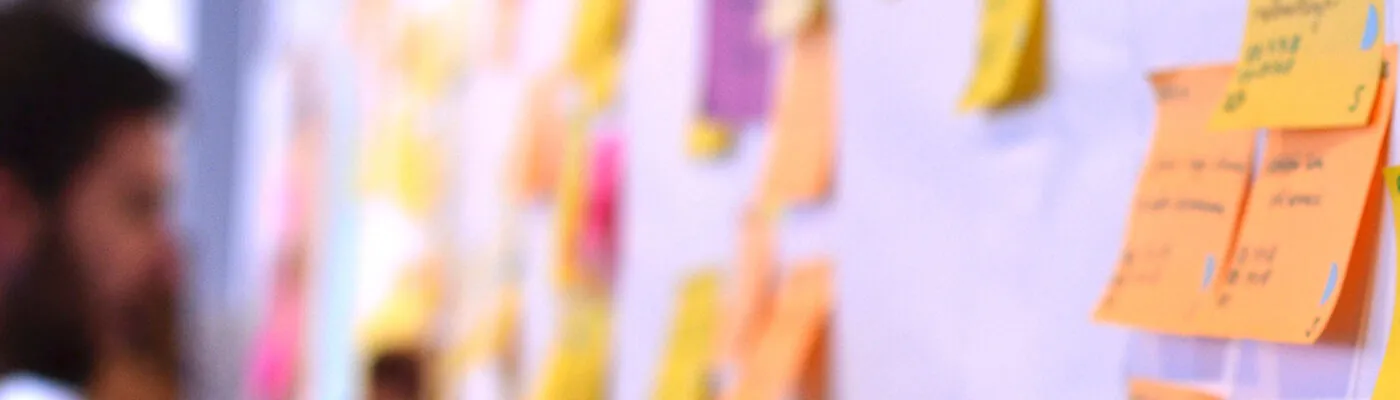 Header image of a slightly out-of-focus man updating a kanban board full of sticky notes.