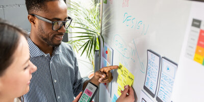 Two designers review their app design goals and mockup on a whiteboard.