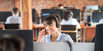 Call center worker accompanied by her team. Smiling customer support operator at work. Young employee working with a headset.