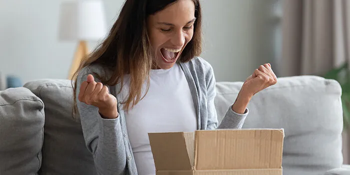 A woman shouts with joy upon opening her box that was just delivered.