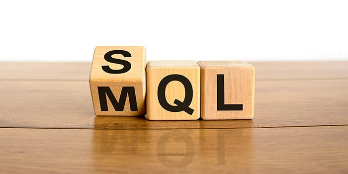 Three wooden blocks spelling out MQL. The "M" block tips over to reveal an "S"